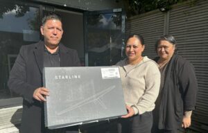 A man holding a Starlink receiver with two women on Matakana Island