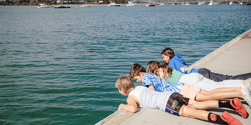 4 school children lying down looking into water - School Based Health Services